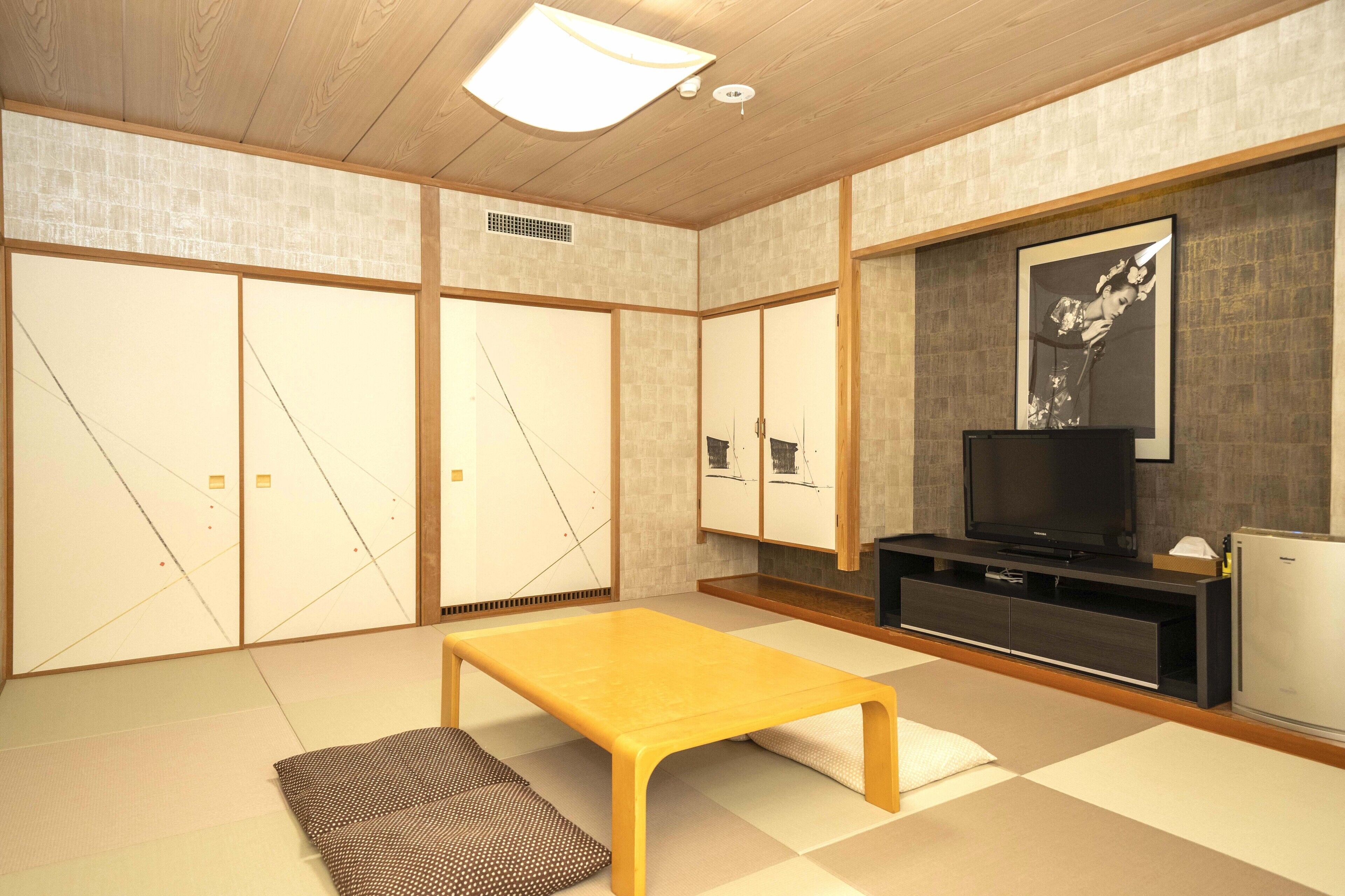 Une pièce de style japonais traditionnel, avec un sol recouvert de tatamis, une basse table en bois, des portes coulissantes en papier de riz (shoji) et un téléviseur posé sur un meuble en bois foncé.