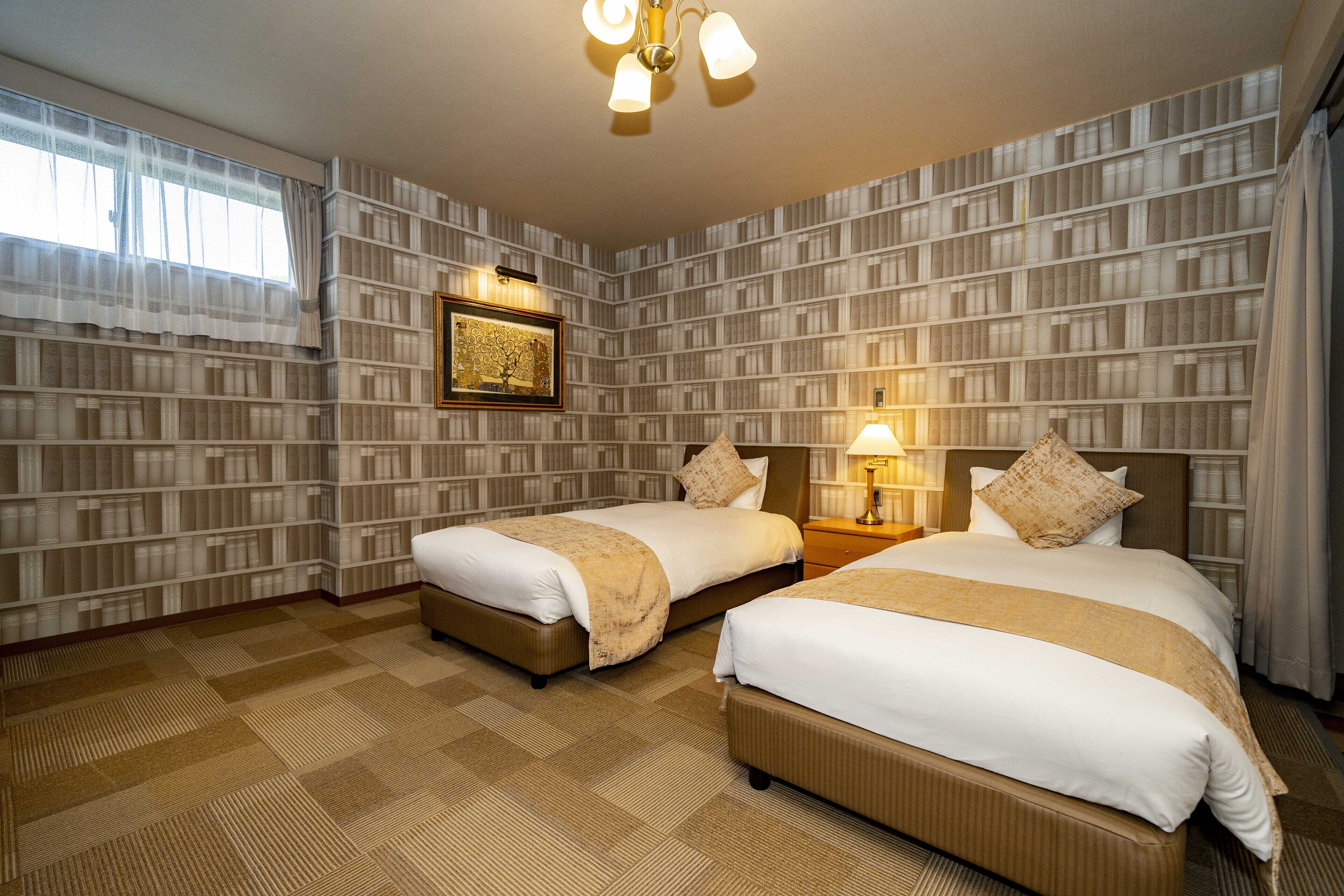 Ein Hotelzimmer mit zwei Betten, einer Kandelaberleuchte, einem gerahmten Bild an der Wand und einem gemusterten Wandteppich.