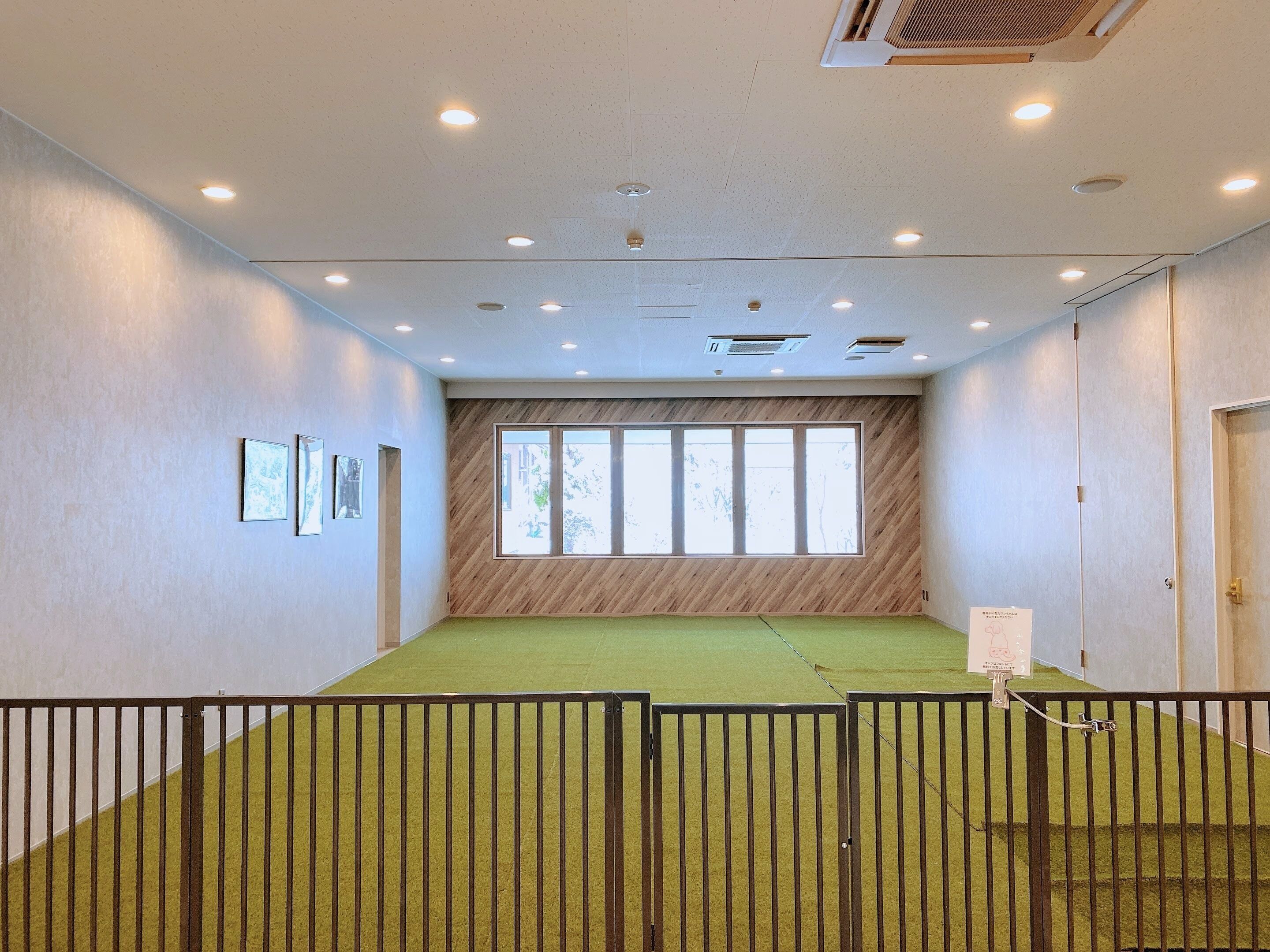 A conference room with a green carpet, wooden panel wall, large windows, and a door.