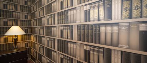 A library with bookshelves filled with books, a lamp, and a dark-colored desk.