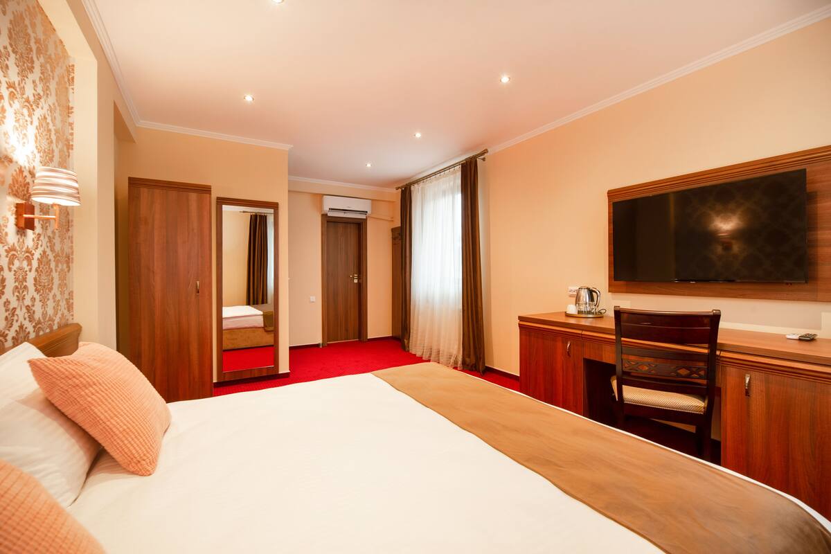 A hotel room with a large bed, a wooden desk, a chair, a television, and a mirror.