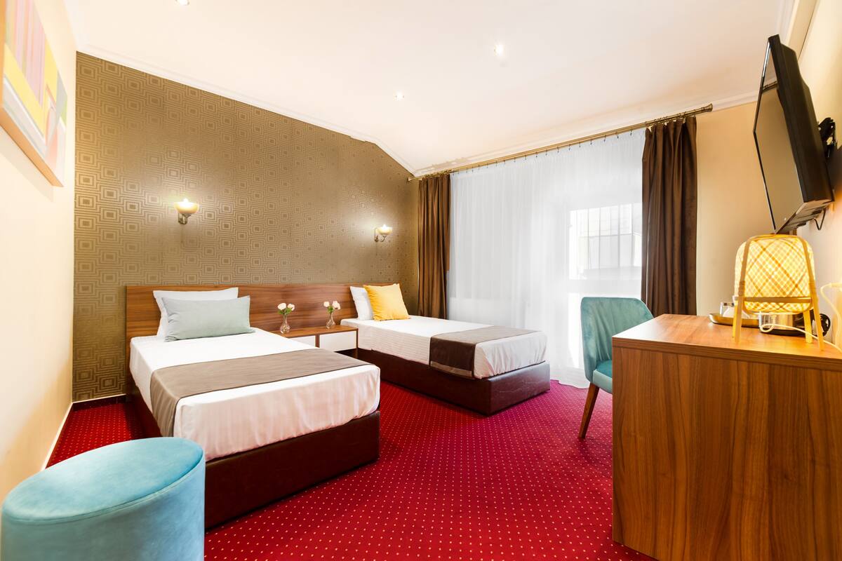 A hotel room with two beds, a desk, a chair, and a TV.