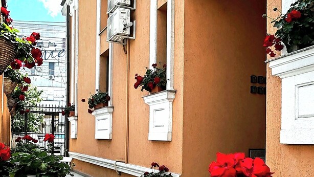 Un edificio con fachada color crema, detalles blancos y numerosos maceteros con flores rojas.