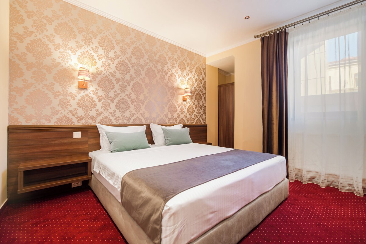 A hotel room with a large bed, two bedside lamps, a wooden headboard, and a red carpet.