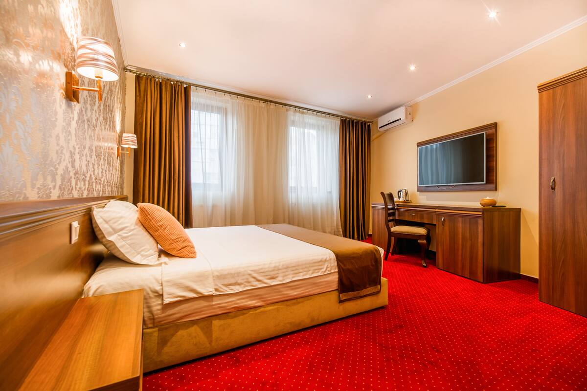 A hotel room with a large bed, a desk, a chair, and a television.