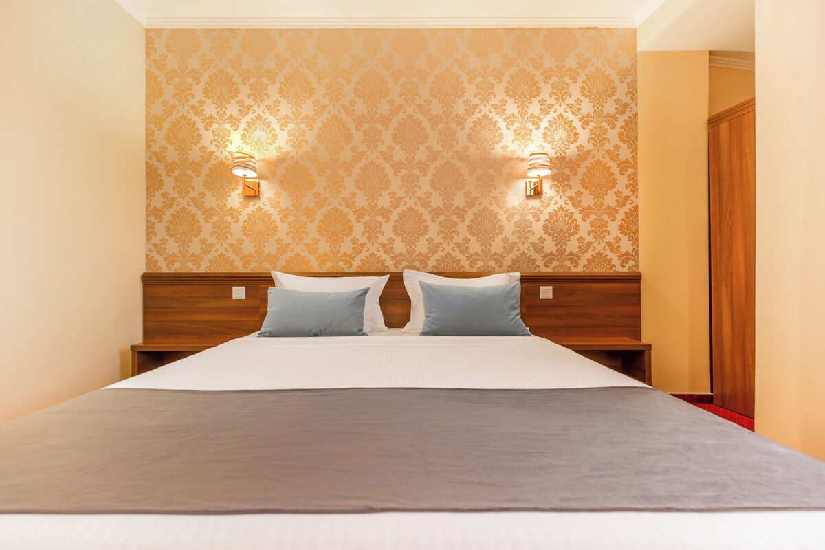 A hotel room with a large bed, two wall-mounted lamps, and a wooden headboard.