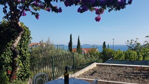 An outdoor dining area with a table set for two, overlooking a garden and a view of the sea. - Apartments Kust (Zupa dubrovacka)