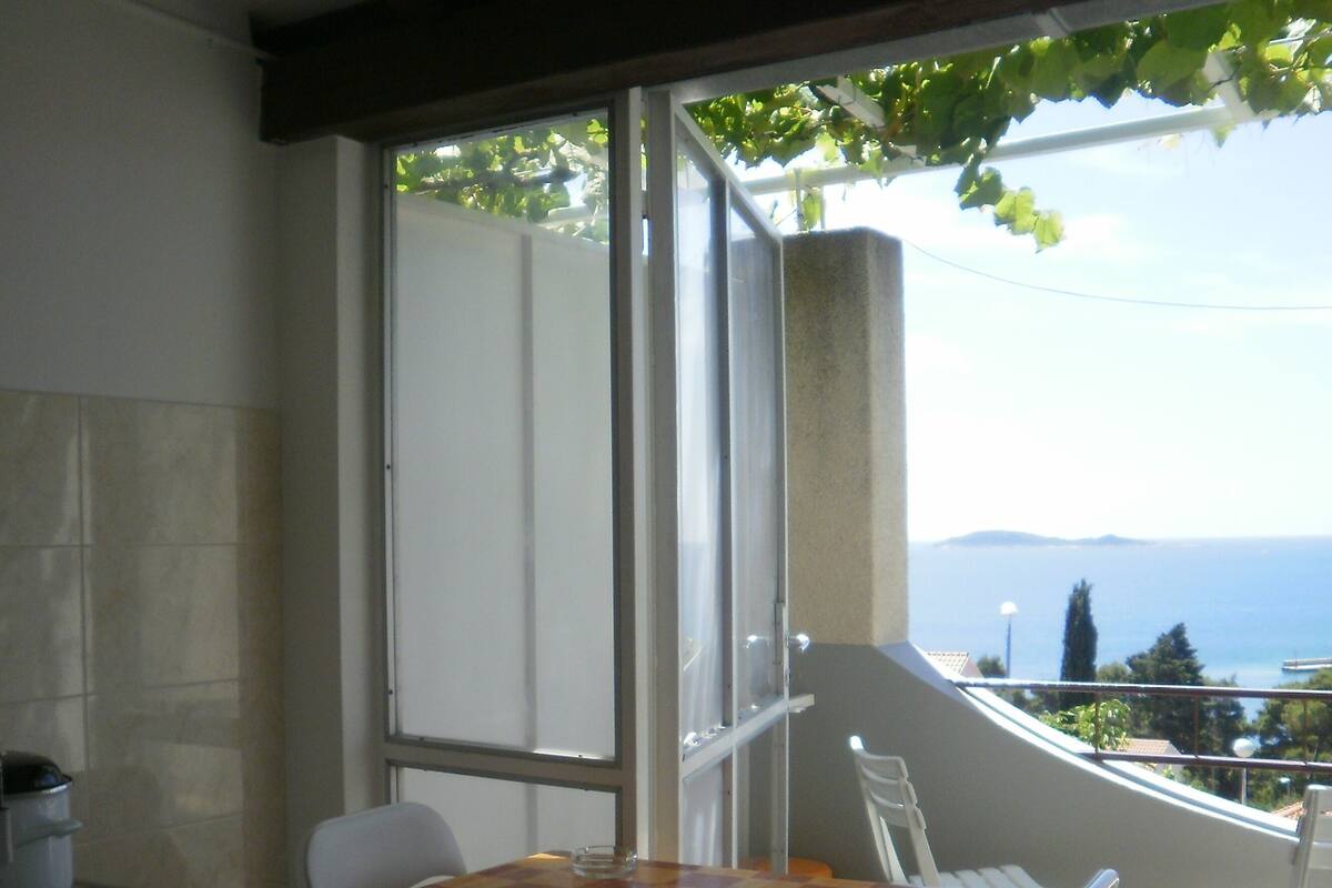 A balcony with a table and chairs, a view of the sea, and a window with a view of the sea.