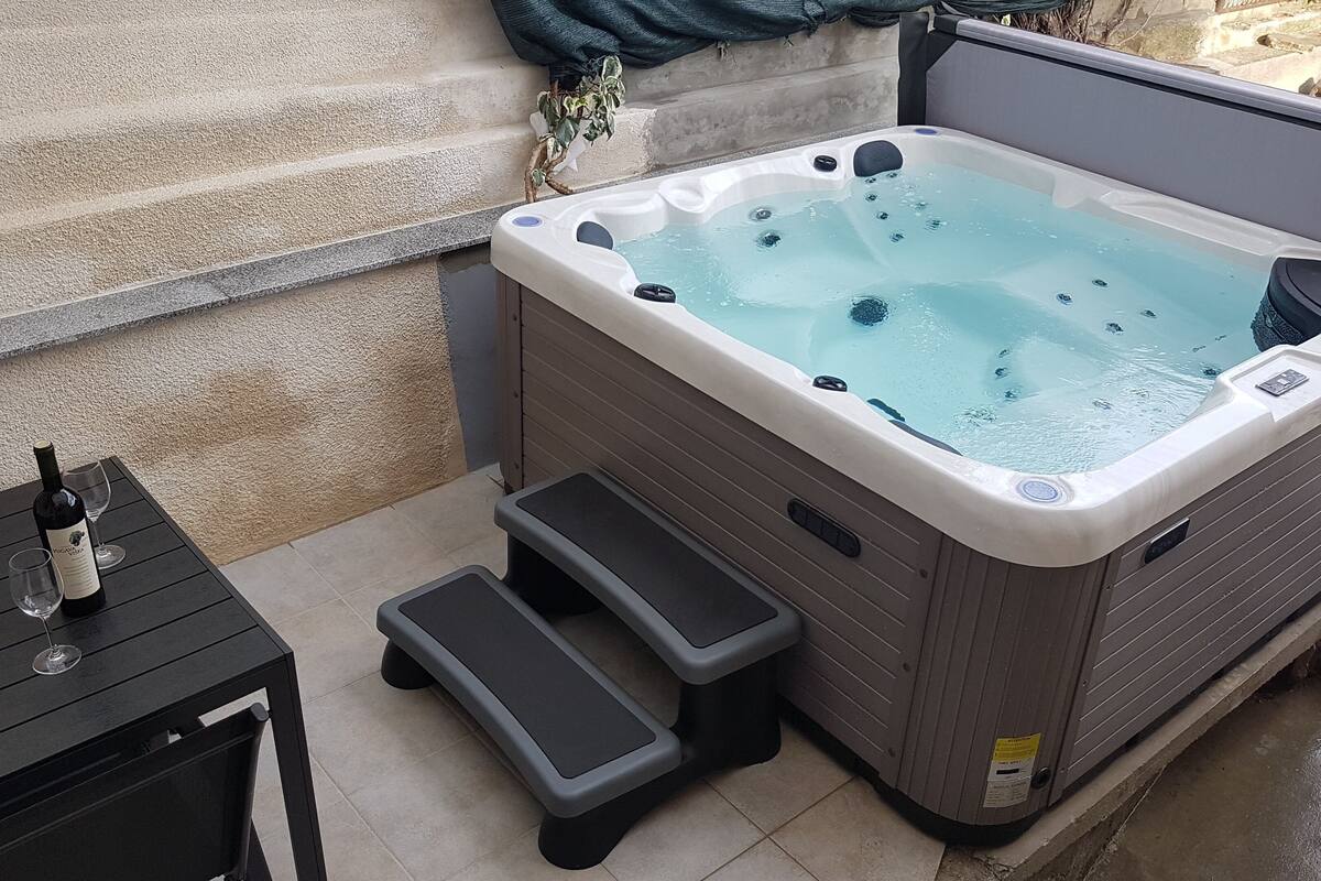 A hot tub with steps leading up to it, a table with a bottle and glasses, and a potted plant.