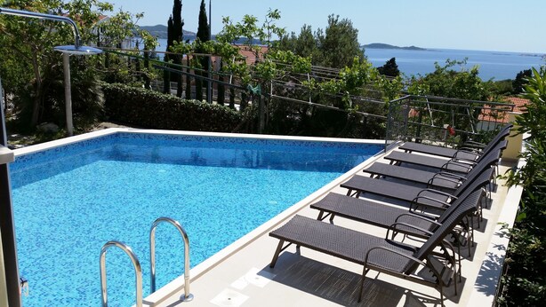 A rectangular swimming pool with a tiled edge, surrounded by lounge chairs and a metal railing. - Apartments Kust (Zupa dubrovacka)