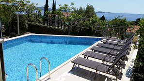 A rectangular swimming pool with a tiled edge, surrounded by lounge chairs and a metal railing. - Apartments Kust (Zupa dubrovacka)