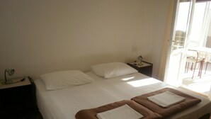 A simple, clean hotel room with a bed, two pillows, a nightstand with a lamp, and a view of the outside balcony. - Apartments Kust (Zupa dubrovacka)