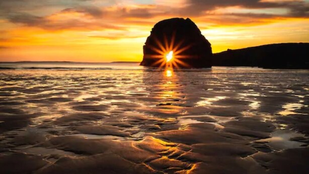 A sunset over a rocky coastline with a prominent rock formation in the center. - Wilde Ballybunion (Ballybunion)