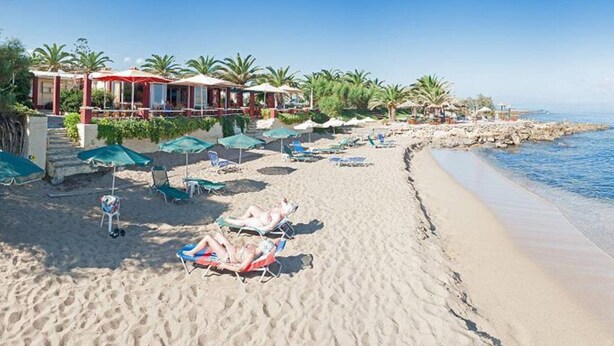 Ein Strand mit Liegestühlen und Sonnenschirmen, ein Gebäude mit rotem Dach und Palmen.