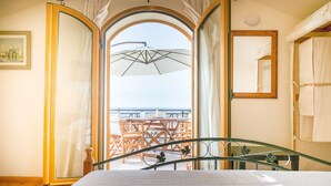 Ein Schlafzimmer mit einem Bett, Holzboden und einer Glastür, die auf einen Balkon mit Gartenmöbeln führt.