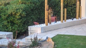 Ein Garten mit einem Betonweg, einer kleinen Sitzgelegenheit und Bambusrohren.