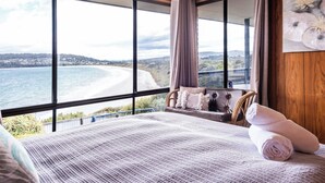 A bedroom with a large window overlooking a beach and hills. - Stones Throw - Holiday Houses Tasmania (Primrose Sands)
