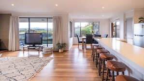 A modern kitchen with a large island, bar stools, and a dining area with a view. - Stones Throw - Holiday Houses Tasmania (Primrose Sands)
