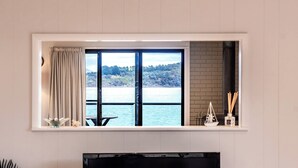 A room with a large window overlooking a body of water, a fireplace, and a small table with decorative items. - Stones Throw - Holiday Houses Tasmania (Primrose Sands)