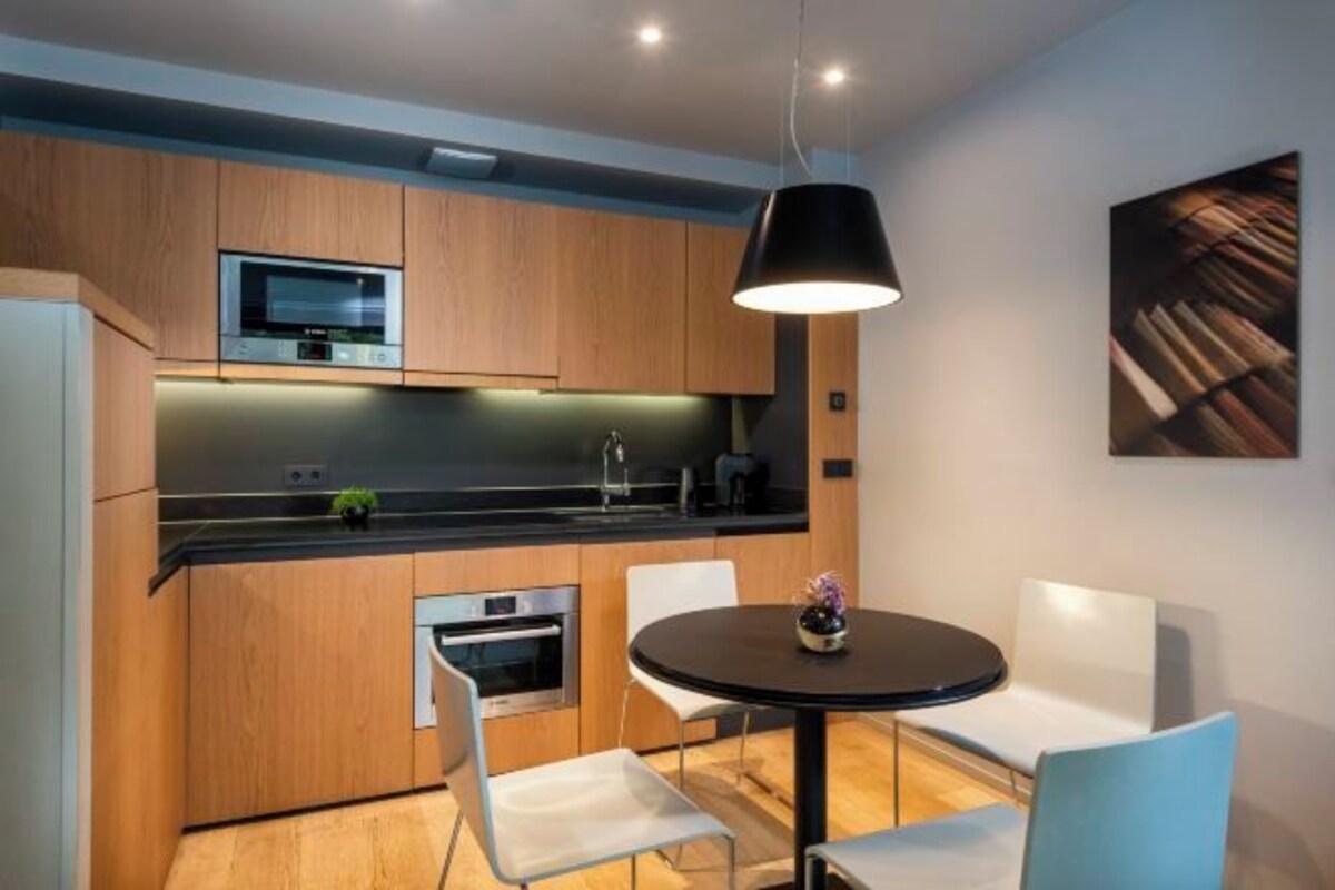 A modern kitchen with wooden cabinets, a black countertop, and a round dining table with white chairs.
