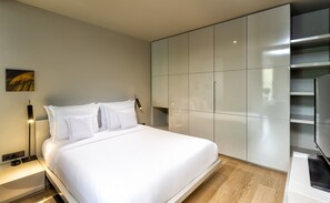 A modern bedroom with a large bed, built-in wardrobe, bedside table, and a wall-mounted lamp.