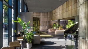 Un hall moderno con un piano de cola, zonas de estar y plantas en macetas.