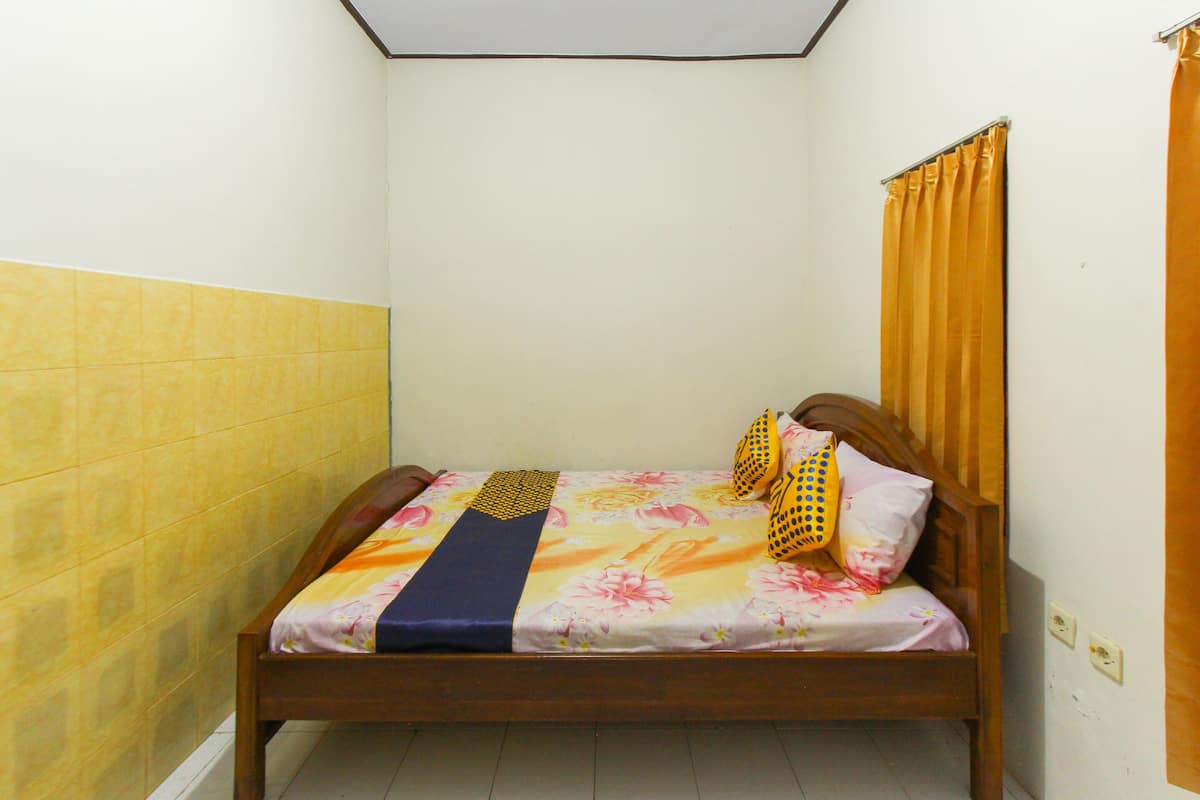 Ein kleines Zimmer mit einem Einzelbett, Holzrahmen, gelb-weißen Wänden und einer blumigen Bettdecke.