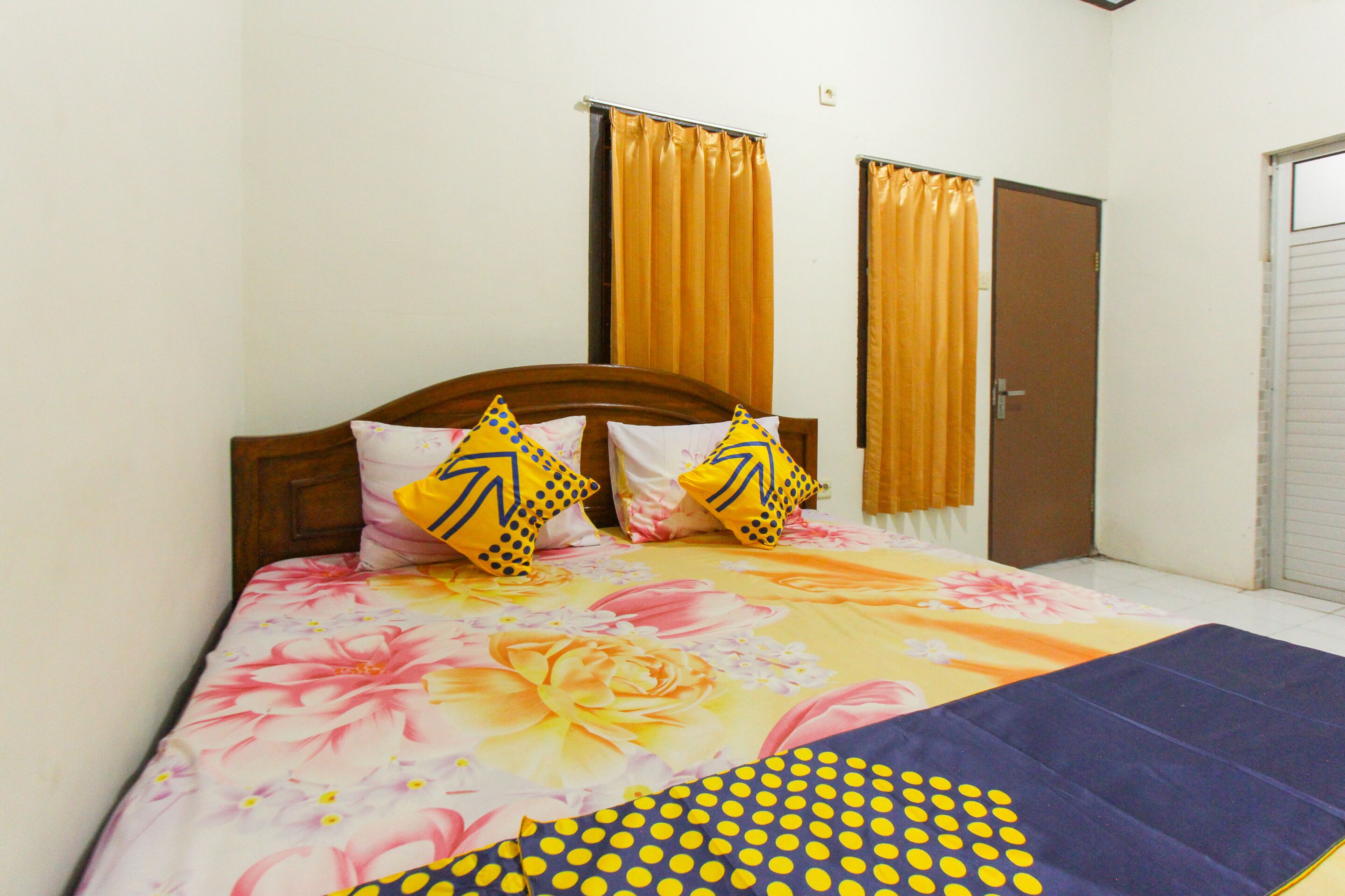 Une chambre à coucher avec une couvre-lit à motifs floraux, deux coussins à motifs géométriques et une couverture bleue.