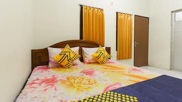 Une chambre à coucher avec une couvre-lit à motifs floraux, deux coussins à motifs géométriques et une couverture bleue.