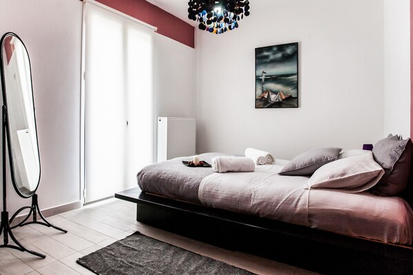 A modern bedroom with a bed, a large mirror, a painting, and a radiator.