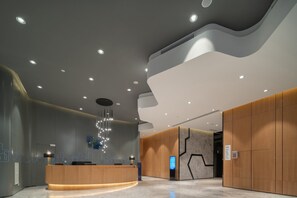 Een moderne receptiezone met een gebogen houten balie, inbouwverlichting en een sierlijke kroonluchter.