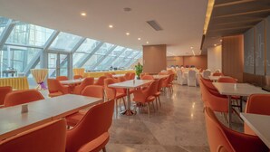 A modern dining area with high ceilings and skylights, featuring orange chairs and white tables. - Holiday Inn Express Qingdao Innovation Park by IHG (Qingdao)