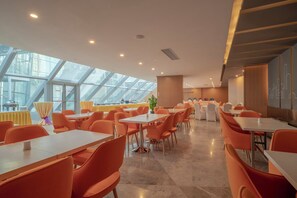 A modern dining area with high ceilings and skylights, featuring orange chairs and white tables. - Holiday Inn Express Qingdao Innovation Park by IHG (Qingdao)