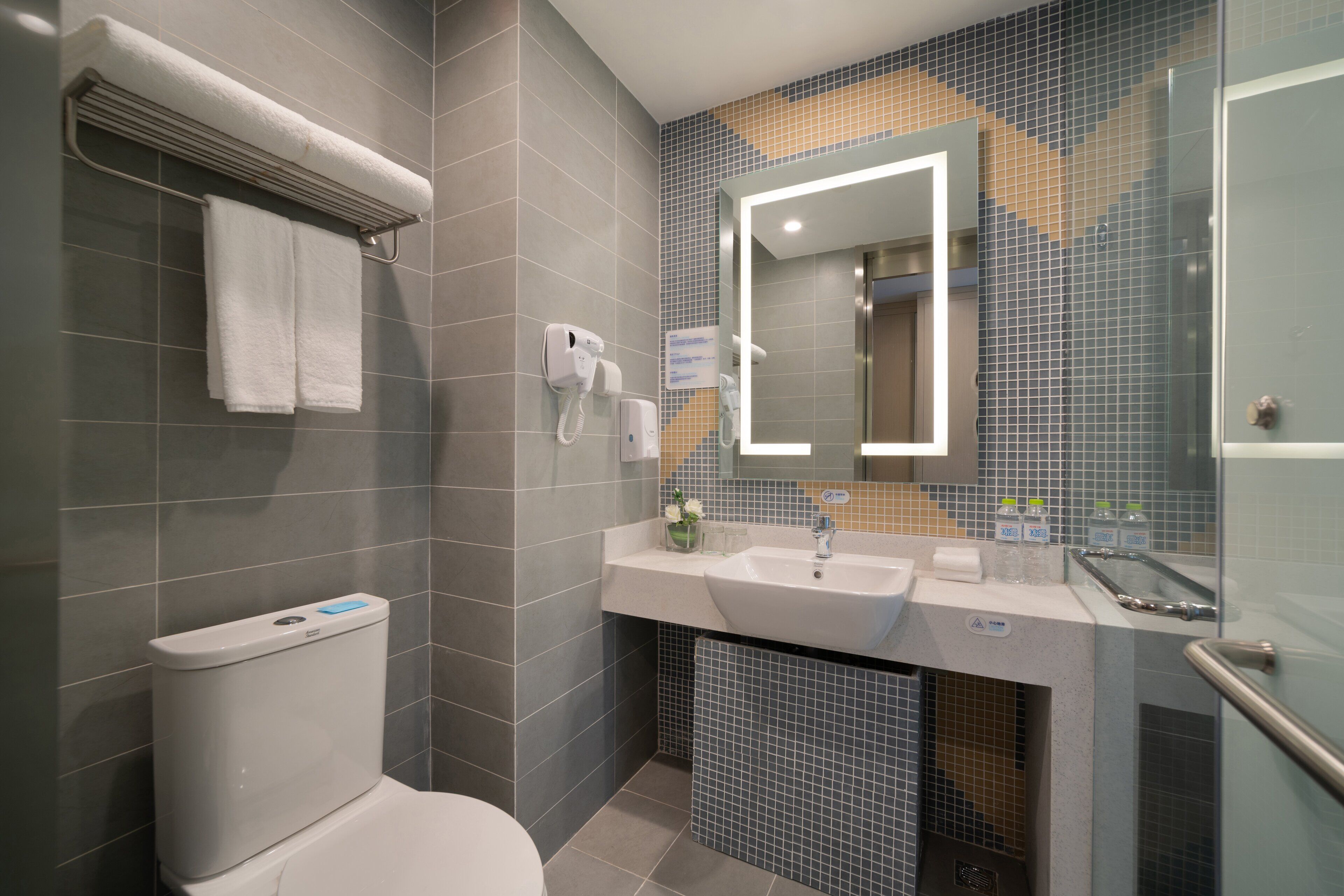 Un baño moderno con inodoro, lavamanos, espejo y toallero.
