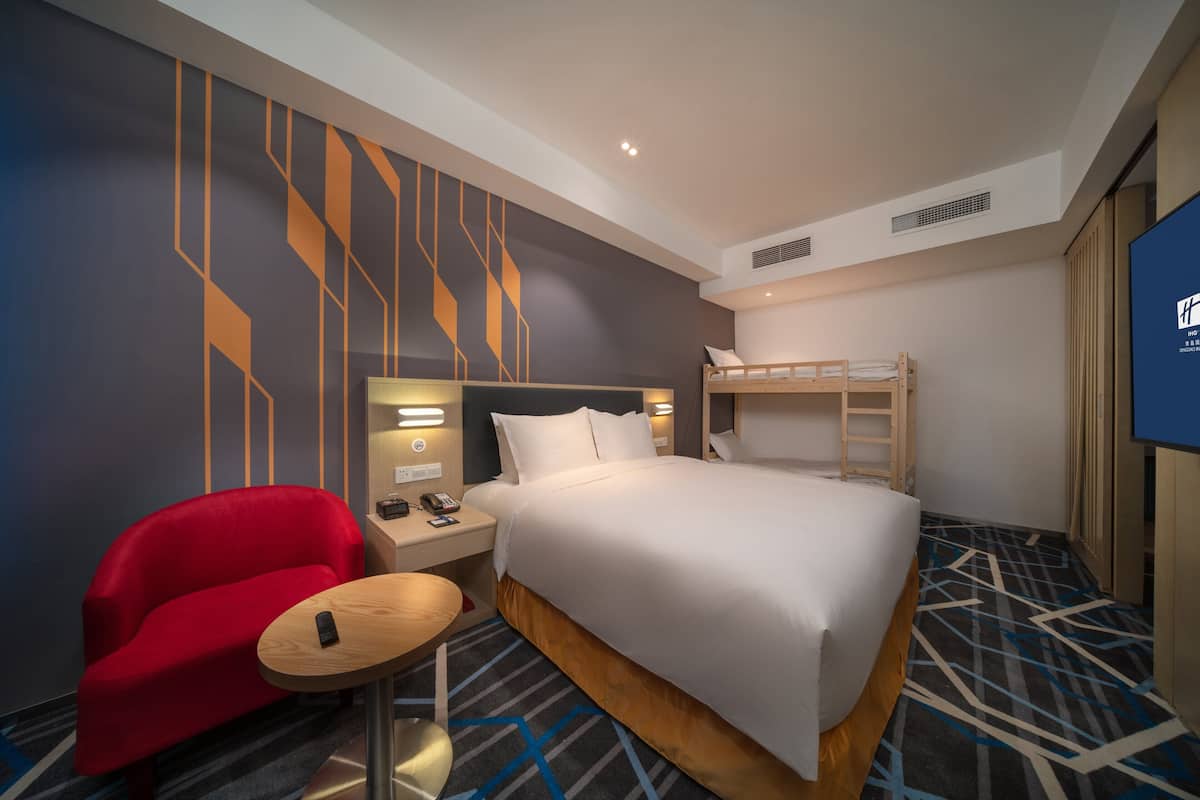 A hotel room with a bunk bed, a red armchair, a small round table, and a TV on the wall.