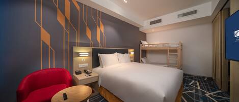 A hotel room with a bunk bed, a red armchair, a small round table, and a TV on the wall.