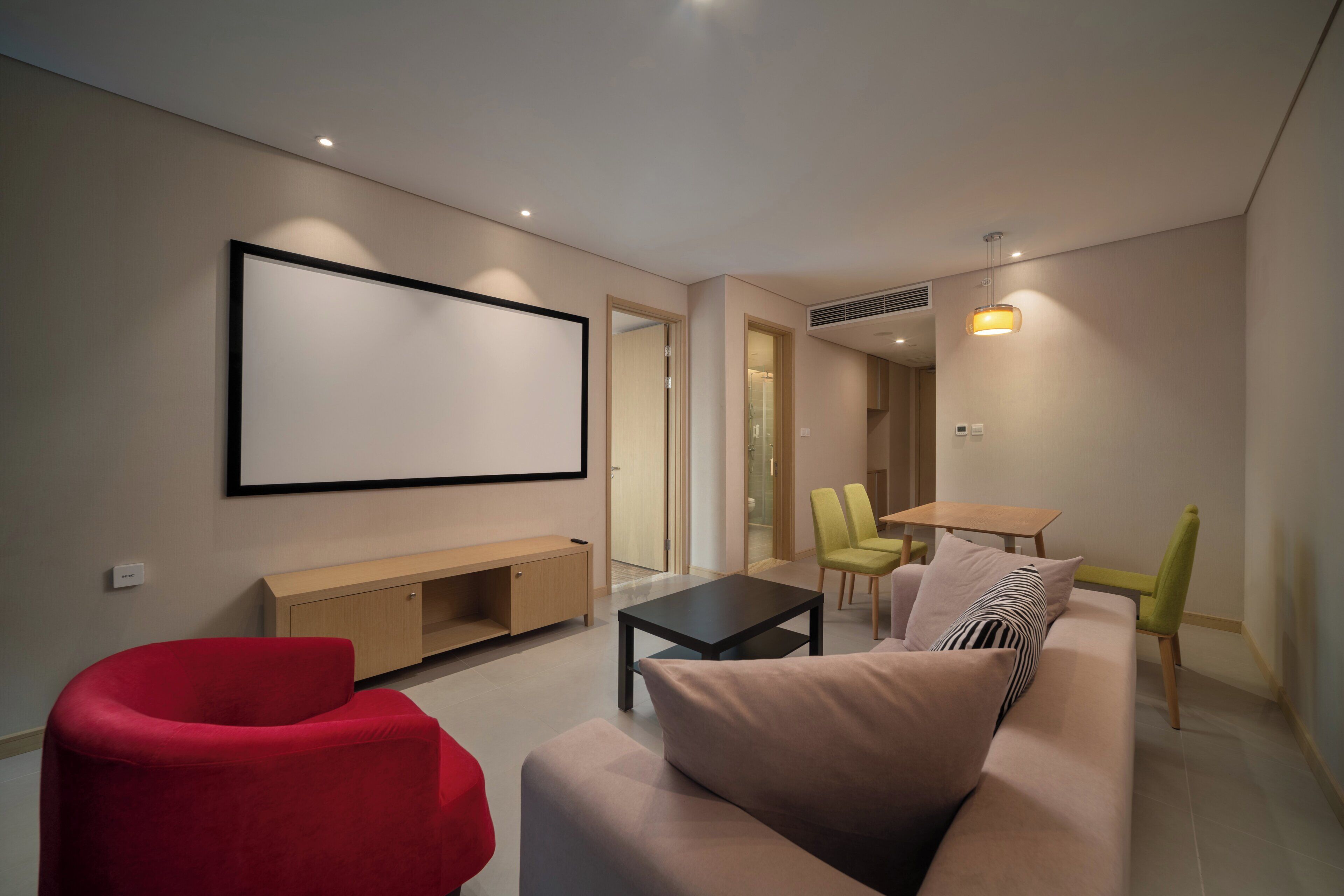 A modern living room with a large flat-screen TV, a sofa, a red chair, a coffee table, and a dining area with chairs and a table.