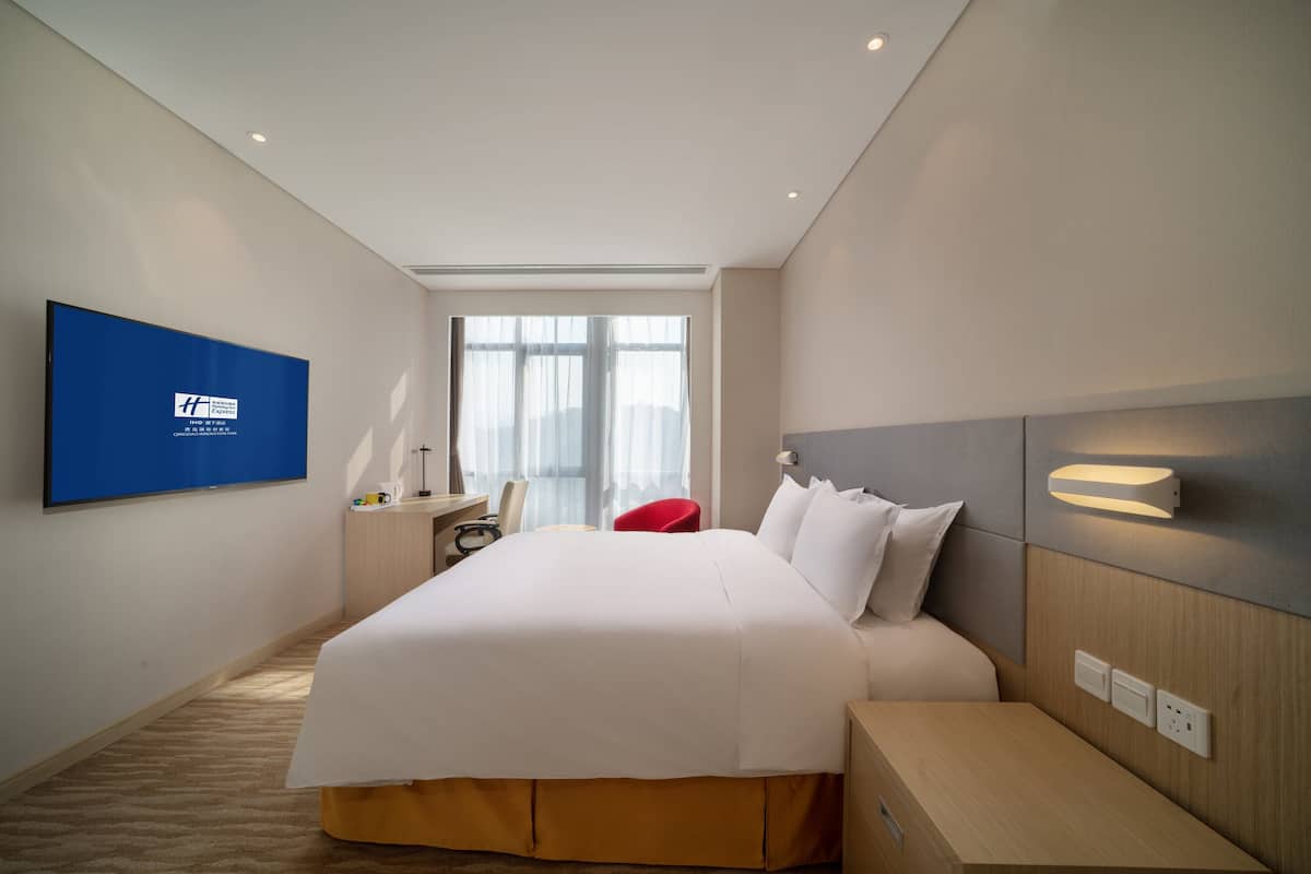 A hotel room with a large bed, a desk, a chair, a TV, and a window.