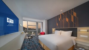 A modern hotel room with a large bed, a desk, and a chair. There is a window with a view of the mountains. - Holiday Inn Express Qingdao Innovation Park by IHG (Qingdao)