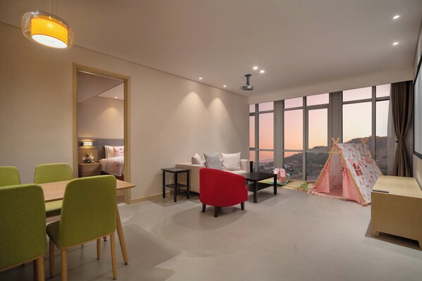 A modern hotel room with a dining area, a bed, a red chair, a small table, a tent, and a large window with a view. - Holiday Inn Express Qingdao Innovation Park by IHG (Qingdao)