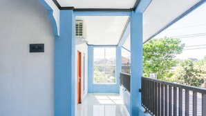 A corridor with blue walls and a white ceiling, leading to a window with a view of greenery and buildings. - Hotel O Homiko (Pacitan)