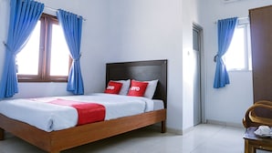 A bedroom with a wooden bed, white bedding, red pillows, and blue curtains. - Hotel O Homiko (Pacitan)