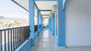 A corridor with blue walls and a tiled floor, leading to a balcony with a black railing. - Hotel O Homiko (Pacitan)