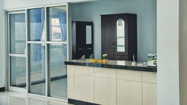 A reception area with a reception desk, a dark wooden cabinet, and a glass door leading to an outdoor area. - Hotel O Homiko (Pacitan)