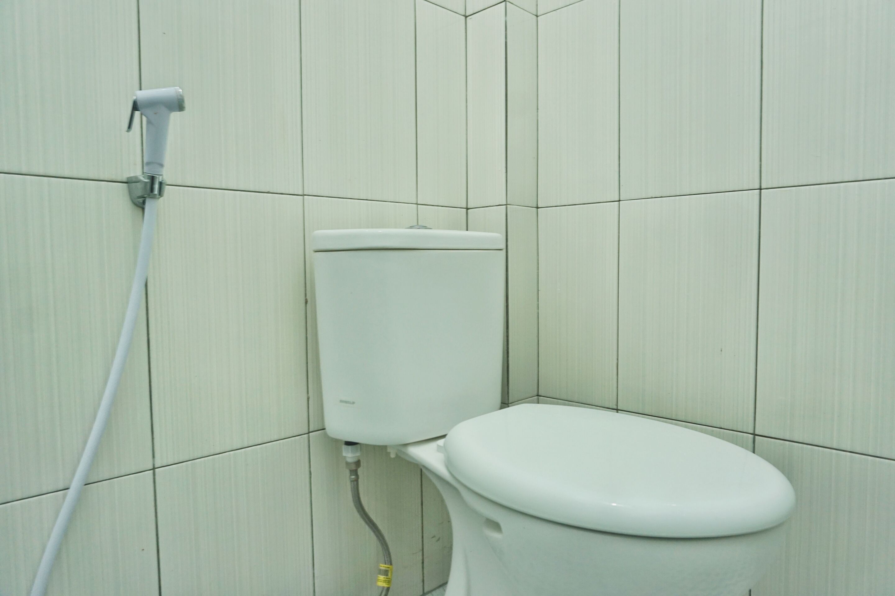 Inodoro con tanque y sistema bidé en un baño con azulejos.