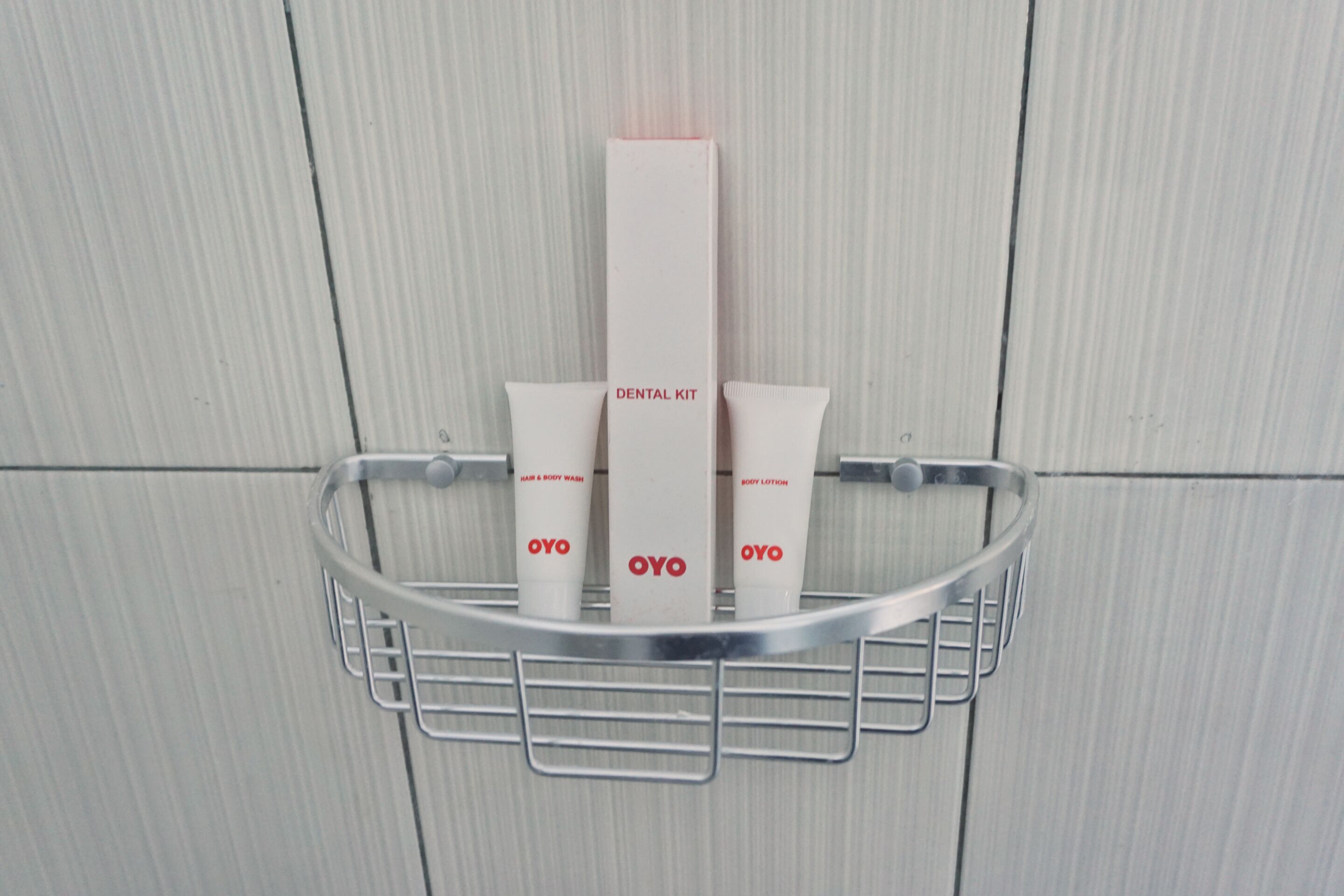 Casa de banho com lavatório de metal, contendo um kit de higiene oral e dois tubos de loção corporal OYO.