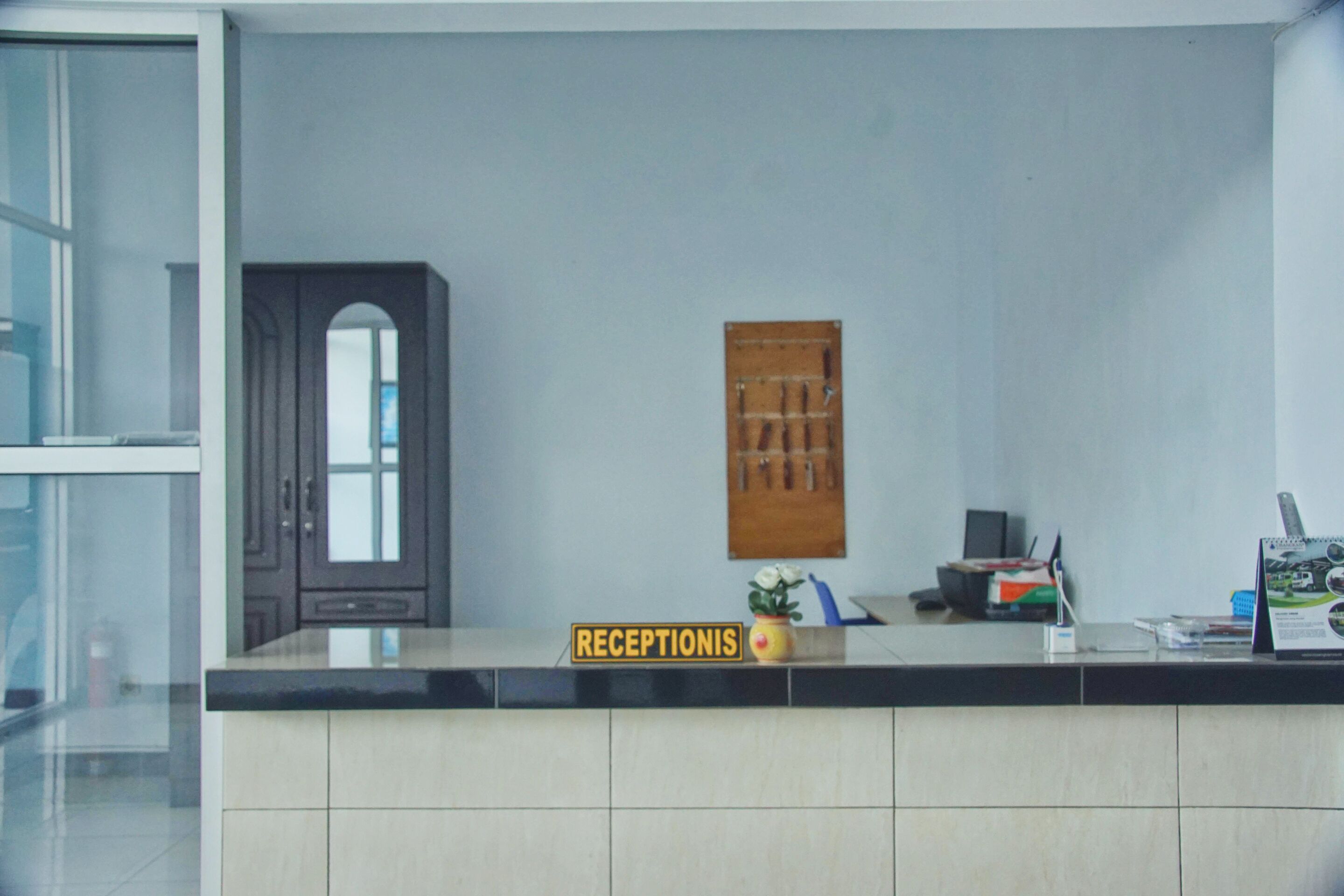 Un área de recepción con un mostrador, un panel de madera y un cartel que dice "RECEPTIONIS".