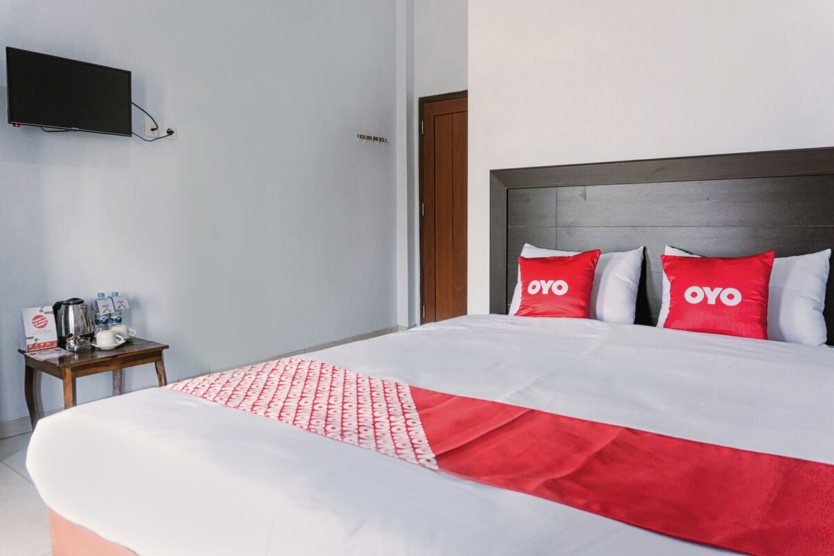 A hotel room with a bed, a TV mounted on the wall, a small table with a coffee maker, and a nightstand.