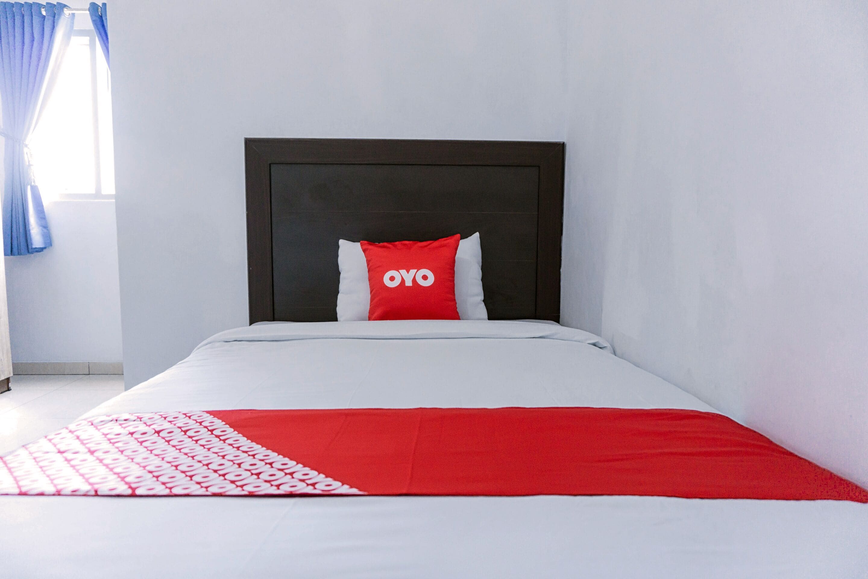 A bed with a white and red bedspread, a dark headboard, and a pillow with 'OYO' text.