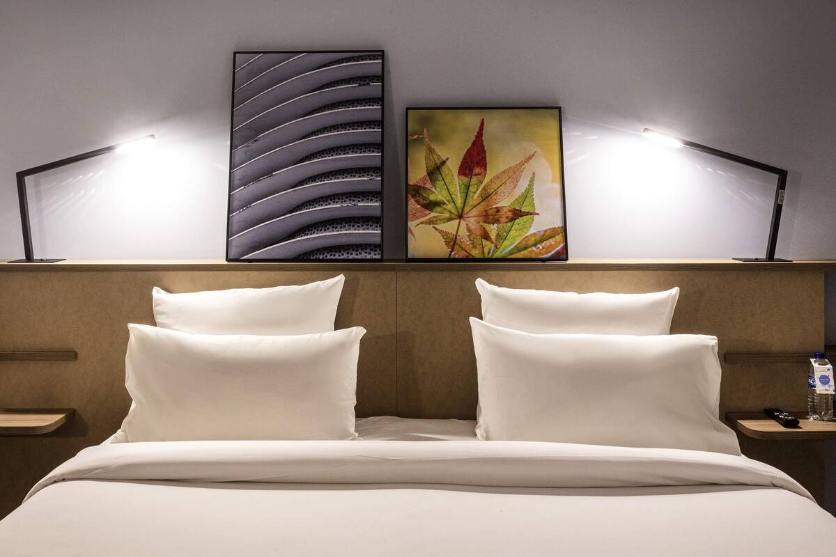 Una habitación de hotel con una cama, dos lámparas de noche, un mesita de noche y dos obras de arte colgadas en la pared.